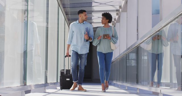 Image of diverse businessman and businesswoman walking with suitcase and talking. business professionals and working in office concept.