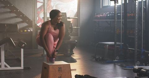 African american woman tying sneaker on plyo box in gym wearing pink workout gear