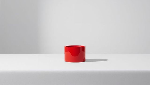 Glossy red cylinder on white cloth table casting soft shadow, minimalist studio still life