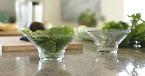 Spinach in glass bowl on granite countertop with minimalist kitchen reflections