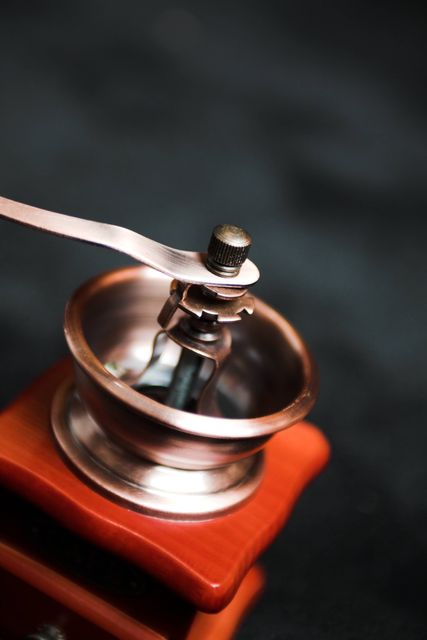 Close-up of vintage manual coffee grinder showing metal parts and wooden base. Suitable for articles, coffee-related websites, educational materials, or advertisements focusing on coffee culture, nostalgia, and traditional coffee-making techniques.