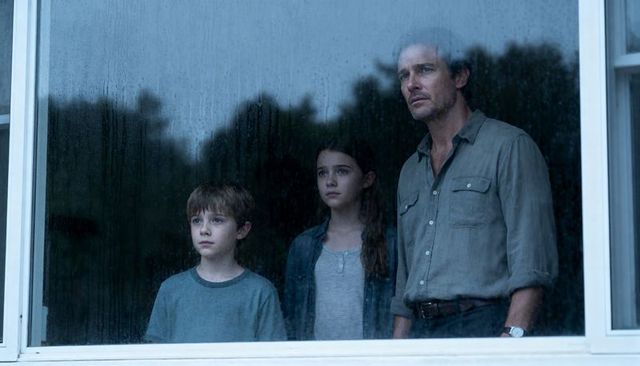 Father and children watching rain through window, moody family moment at home