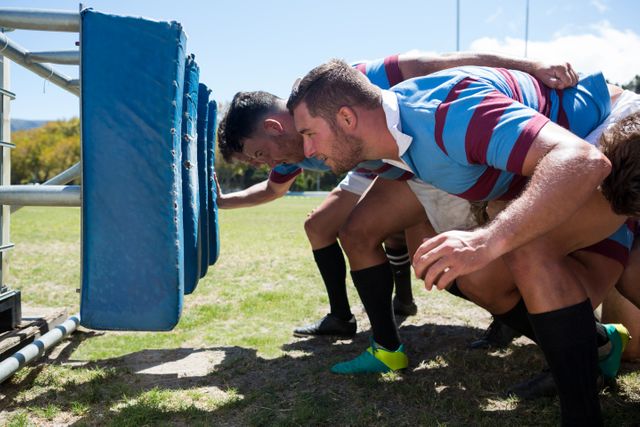 Side view of rugby players crouching at field on sunny day