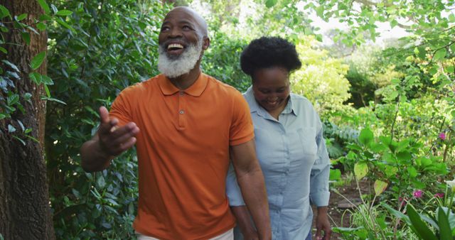 Senior African American couple enjoying a joyful walk through a lush garden, embracing nature and spending quality time together. Perfect for use in promotions of healthy aging, lifestyle, togetherness, retirement living, wellness retreats, and nature-related activities.