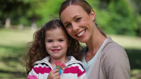 Smiling Mother and Daughter Holding Flower in Park