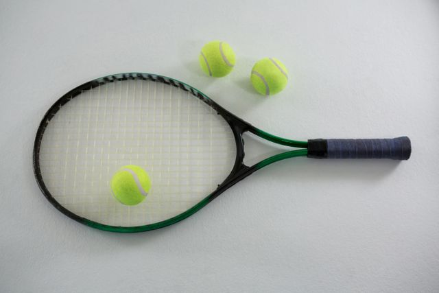 This image shows an overhead view of a tennis racket and three tennis balls on a white background. It is ideal for use in sports-related content, fitness blogs, recreational activity promotions, and advertisements for tennis equipment. The clean and simple composition makes it suitable for various design projects and marketing materials.