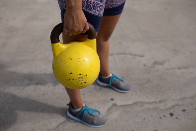 Side view low section of a strong Caucasian woman wearing sportswear exercising outdoors by the seaside on a sunny day, strength training holding yellow kettlebell.