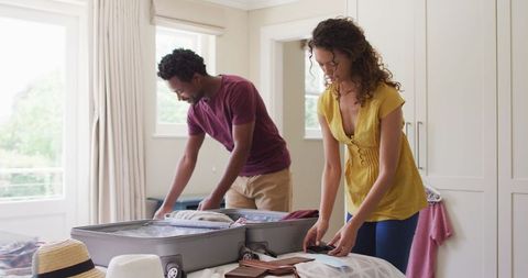 Happy biracial couple packing clothes for vacation travel