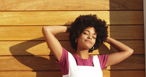 Smiling Woman Basking in Warm Sunlight by Wooden Wall