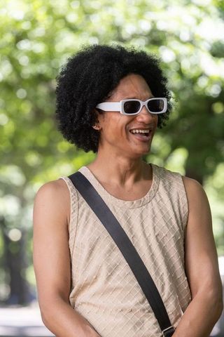 African american man smiling in park wearing white sunglasses and beige sleeveless top