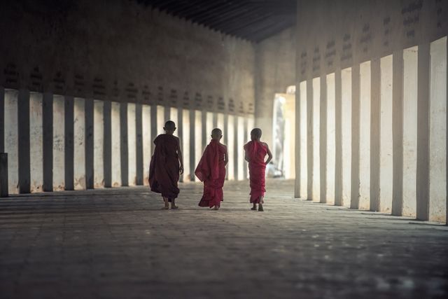 Three young Buddhist monks are walking through a serene monastery corridor. The image captures the cultural and spiritual essence of Buddhist monastic life. It conveys a sense of peace, reflection, and spirituality, making it suitable for topics related to culture, religion, spirituality, and travel. Ideal for blogs, articles, or educational materials about Buddhism and monastic traditions.