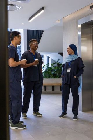 Healthcare team taking coffee break in modern hospital lobby near elevator wearing navy scrubs