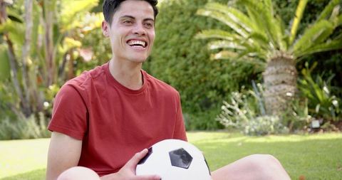 Joyful Man with Soccer Ball Sitting in Lush Green Garden