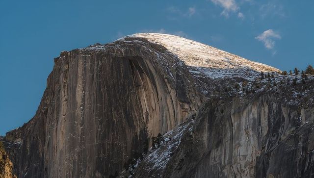 Sunlit granite dome with snowy summit and vertical rock faces in alpine mountain landscape