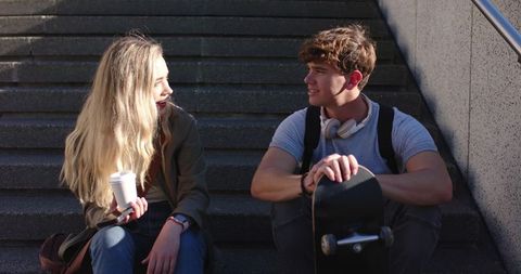 Young Couple Sitting on Urban Steps Talking Over Coffee and Skateboard