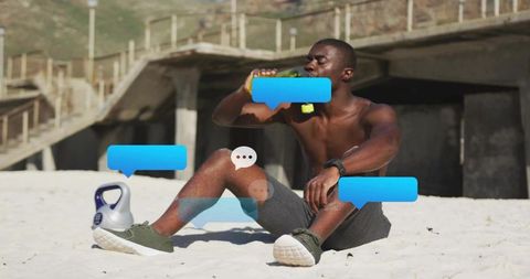 Shirtless man resting on beach after workout drinking water with kettlebell by foot