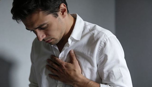 Man pressing hand to chest looking down in white shirt conveying pain and quiet reflection