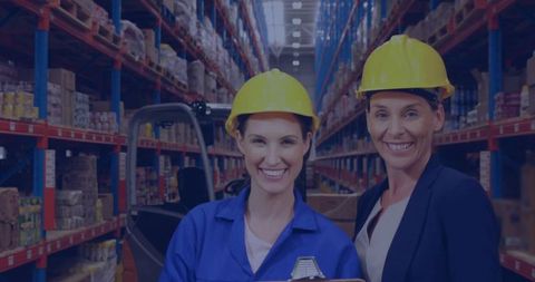 Two Women Supervising Warehouse Operations Wearing Yellow Hard Hats Holding Clipboard