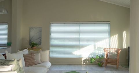 Sunlight casting diagonal pattern through closed white blinds in minimal living room