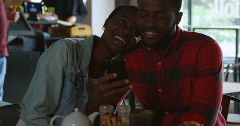 Couple Sharing a Joyful Moment on Smartphone at Cafe