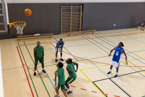 Diverse male basketball players jumping and contesting rebound near hoop on indoor court