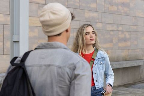 Young couple pausing on urban sidewalk, woman in denim jacket holding phone, casual city style