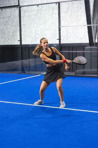 Female athlete playing padel on indoor blue court in black sportswear