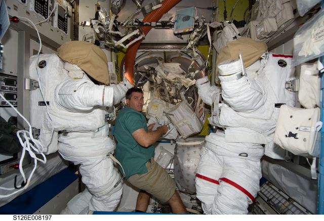 S126-E-008197 (19 Nov. 2008) --- Astronaut Steve Bowen, STS-126 mission specialist, works in the Quest Airlock of the International Space Station while Space Shuttle Endeavour is docked with the station. Two Extravehicular Mobility Unit (EMU) spacesuits are visible in the image.