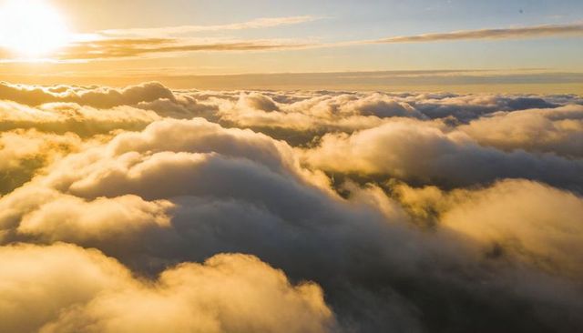 Golden Sunrise Over Cumulus Sea: Aerial Cloudscape Bathing in Warm Light Soft Horizon Glow