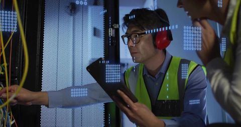 Asian Technician Inspecting Server Rack and Troubleshooting Network Cables with Tablet