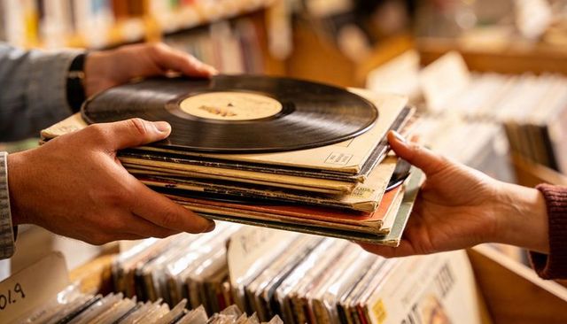 Two adults exchanging vintage vinyl records at cozy record store passing lps and sleeves