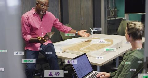 Design lead discussing terrain model with colleague, reviewing blueprint and wind turbine