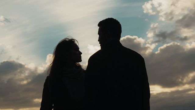 Silhouetted couple facing each other against dramatic sunset sky and textured cloudscape