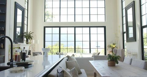 Sunlit minimalist open-plan living and dining with black grid windows and warm wood