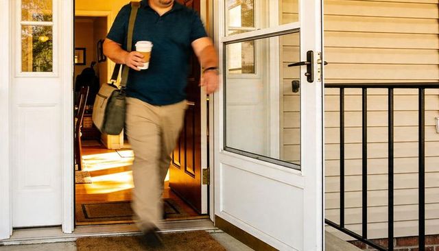 Man walking out of home with coffee and messenger bag leaving for work in morning light