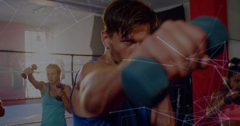 Focused boxer training with dumbbell in group intense boxing fitness class inside gym