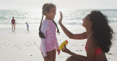 Mother applying sun cream to daughter on sunny beach