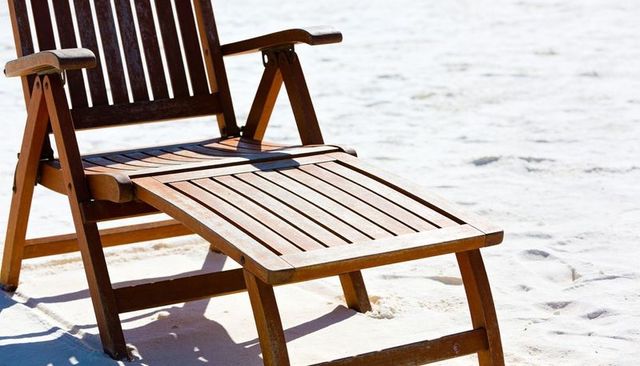Sunlit wooden reclining beach lounger casting sharp shadow on white sand for relaxation