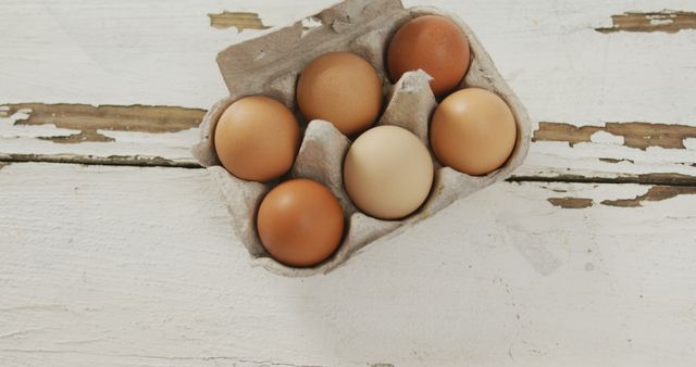 Collection of six brown organic eggs resting in carton on rustic wooden table. Suitable for advertising farm-fresh produce, health and nutrition blogs, recipe websites, countryside living magazines, and organic lifestyle promotions.