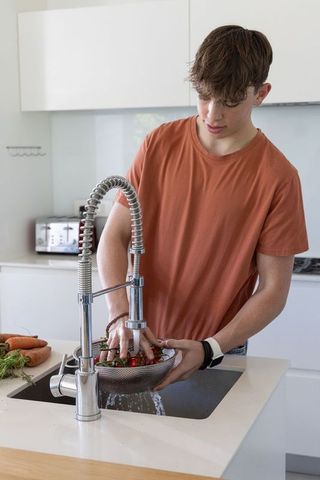 Teen washing strawberries in modern kitchen sink with spring-coil faucet, metal colander
