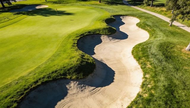 Contoured sand bunker snaking along manicured putting green with flagstick on golf course