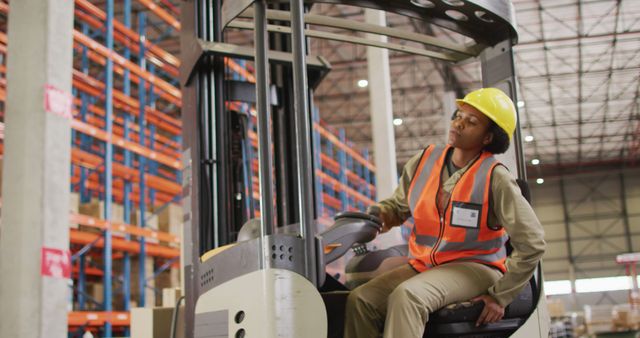 African american female worker wearing safety suit and sitting in turret truck in warehouse. global business, shipping and delivery.
