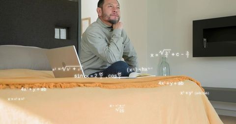 Contemplative asian man studying math on laptop in modern minimalist bedroom