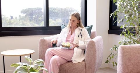 Female medical professional taking break in clinic wearing stethoscope eating salad