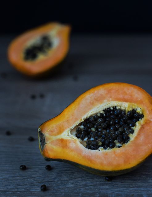 Close-up view of ripe papayas cut open exposing their black seeds, set on a wooden surface. Ideal for use in food blogs, health and nutrition websites, and organic food promotions, it visually highlights the freshness and nutritional benefits of this tropical fruit.
