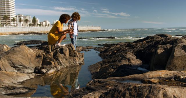 Mother and child enjoy sunny day together exploring rocky beach. Perfect for themes on family bonding, nature adventures, coastal recreation, or travel and tourism. Suitable for illustrating family activities, outdoor hobbies, or vibrant scenic destinations.