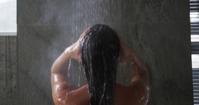 Woman standing under a shower with her head tilted back and hands on her head. The setting suggests privacy and relaxation, making it ideal for ads promoting personal care products, spa treatments, and hygiene-related topics.
