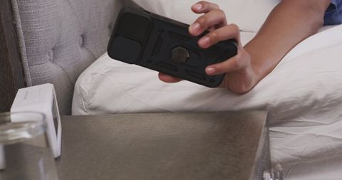 African american woman reaching for rugged smartphone on nightstand with alarm clock