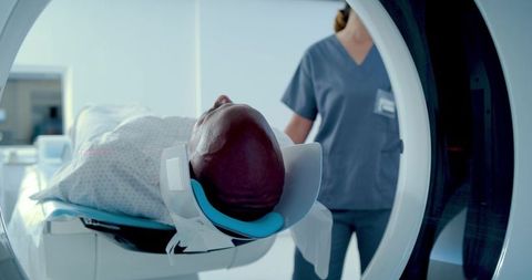 Patient receiving mri brain scan while technician monitoring head coil in radiology suite