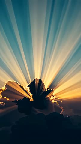 Sun breaking through central cloud sending golden crepuscular rays across vertical dawn sky